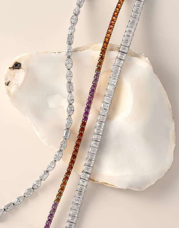Three diamond bracelets with different colored gemstones on a shell.