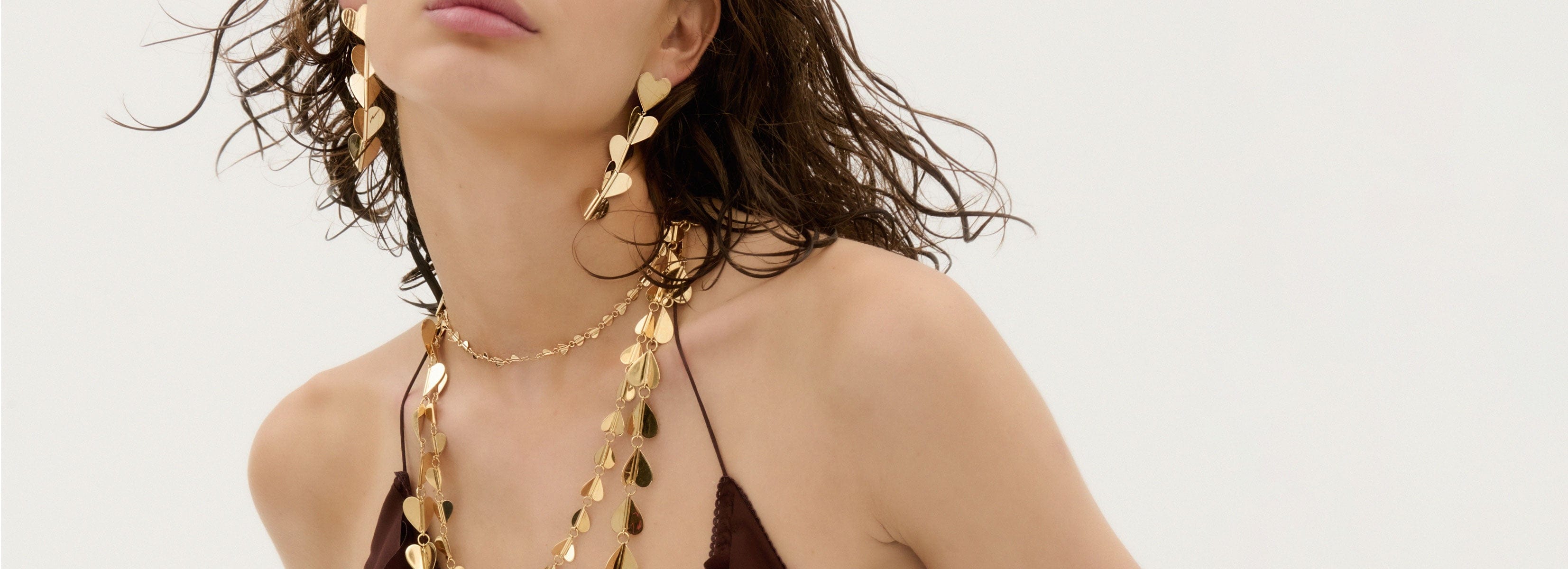 Woman wearing a gold necklace and earrings on a plain background