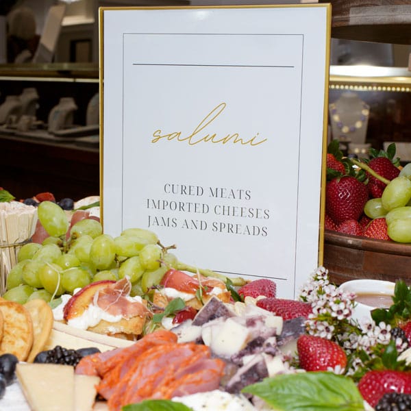 Charcuterie board with salumi sign, fruits, and cheeses.