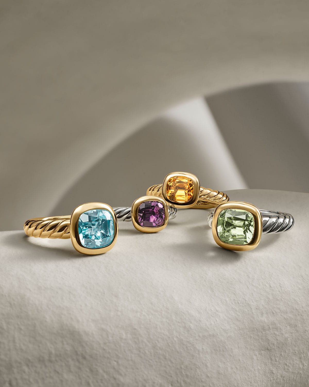 Four gold David Yurman cable rings with colorful gemstones on a light background.