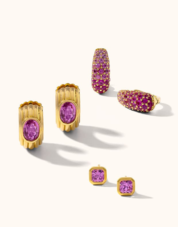 A set of gold jewelry pieces featuring oval and rectangular purple gemstones, arranged on a clean off-white background with soft shadows.
