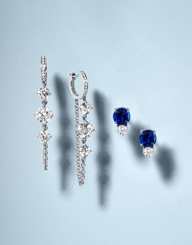 Pair of diamond earrings and a blue gemstone earring on a light gray background