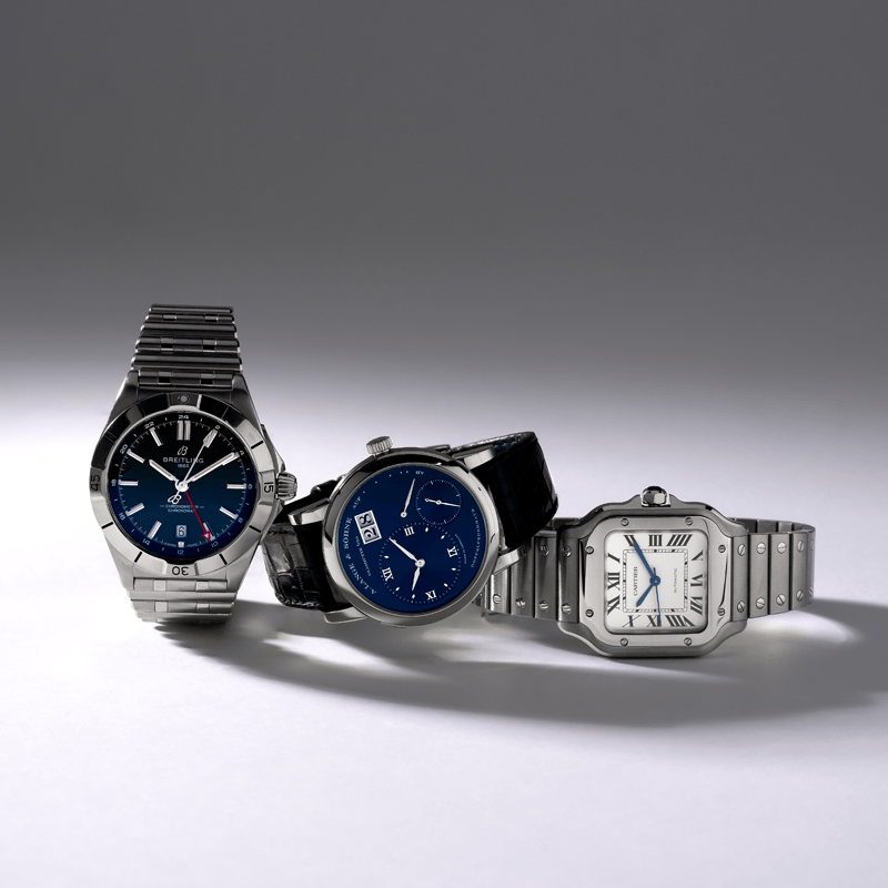 Three luxury watches from Breitling, A. Lange & Sohne, and Cartier displayed against a gradient gray background