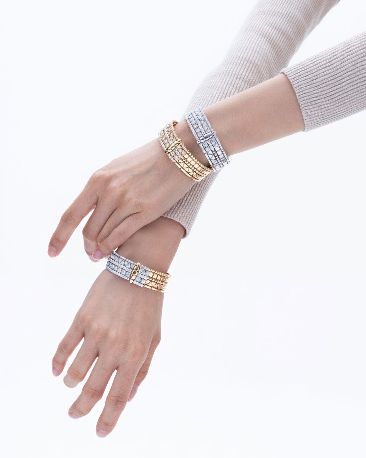 Two hands wearing gold and silver bracelets on a white background