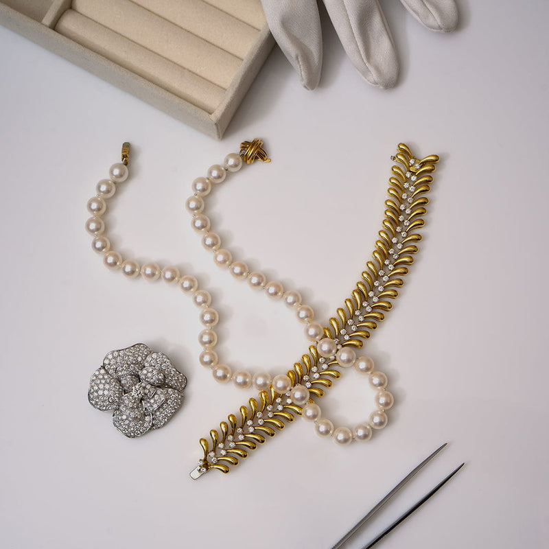 Pearl necklace with gold accents and a brooch on a light surface.