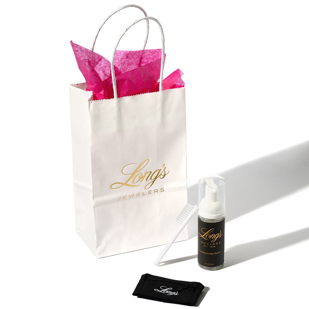 Long's Jewelers gift bag with pink tissue paper, bottle, comb, and pouch on a white background.