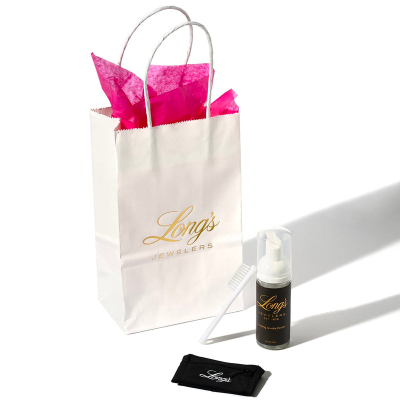 Long's Jewelers gift bag with pink tissue paper, bottle, comb, and pouch on a white background.