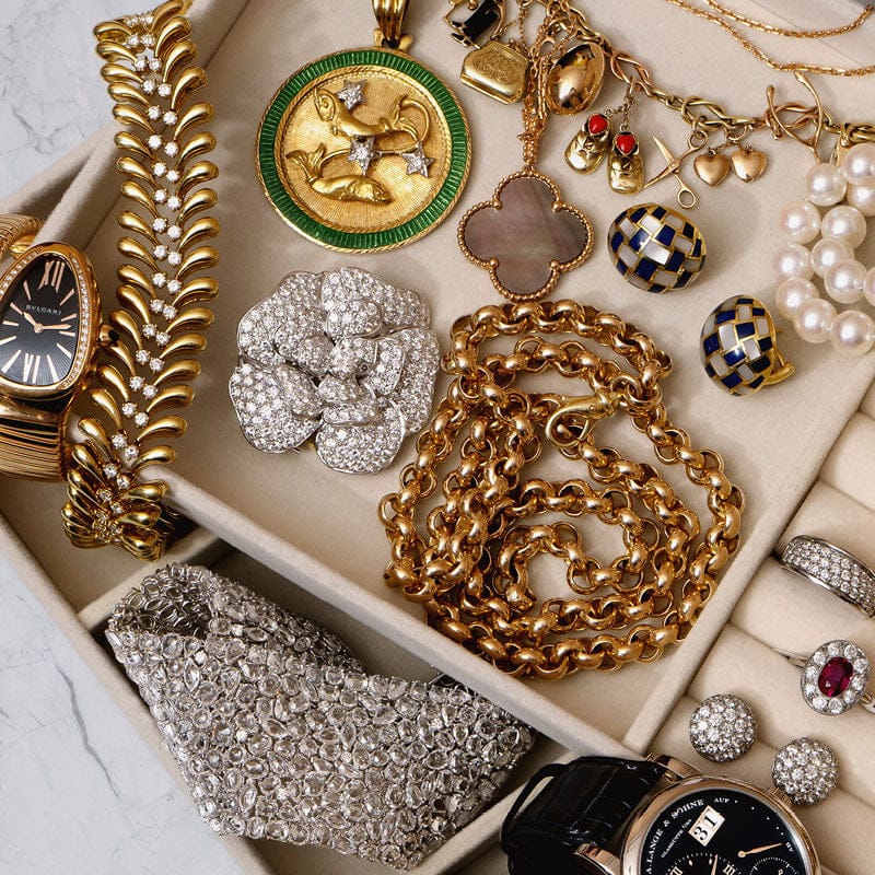 Assorted vintage jewelry including watches, necklaces, and earrings on a marble surface.