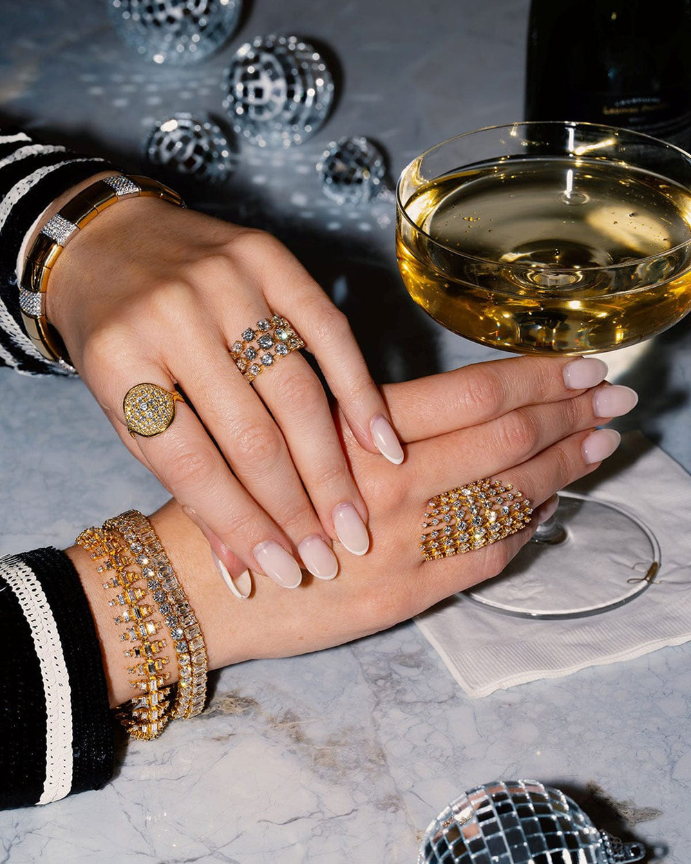 Hand with jewelry holding a glass of white wine on a marble surface