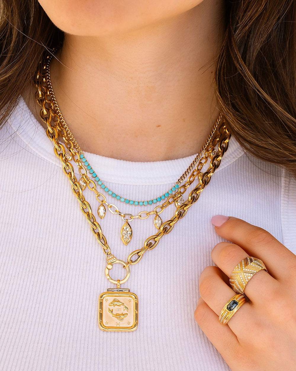 Close-up of a person wearing multiple gold necklaces and rings on a white background