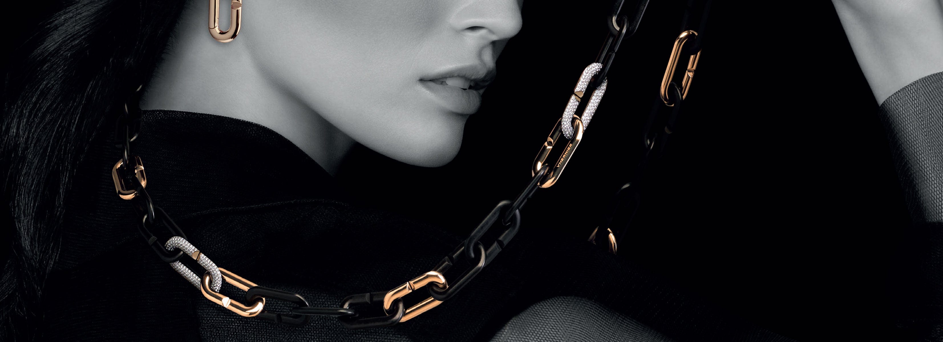 Close-up of a model for Vhernier wearing a black outfit with gold chain details against a dark background