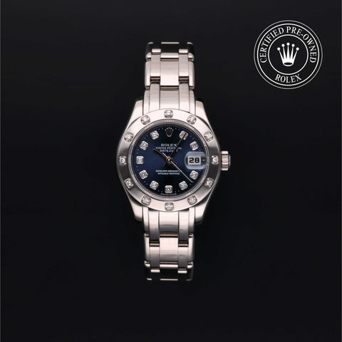 A silver watch with a blue dial displaying the date, adorned with diamonds around the bezel. The background is black with a Certified Pre-Owned Rolex logo in the top right corner.