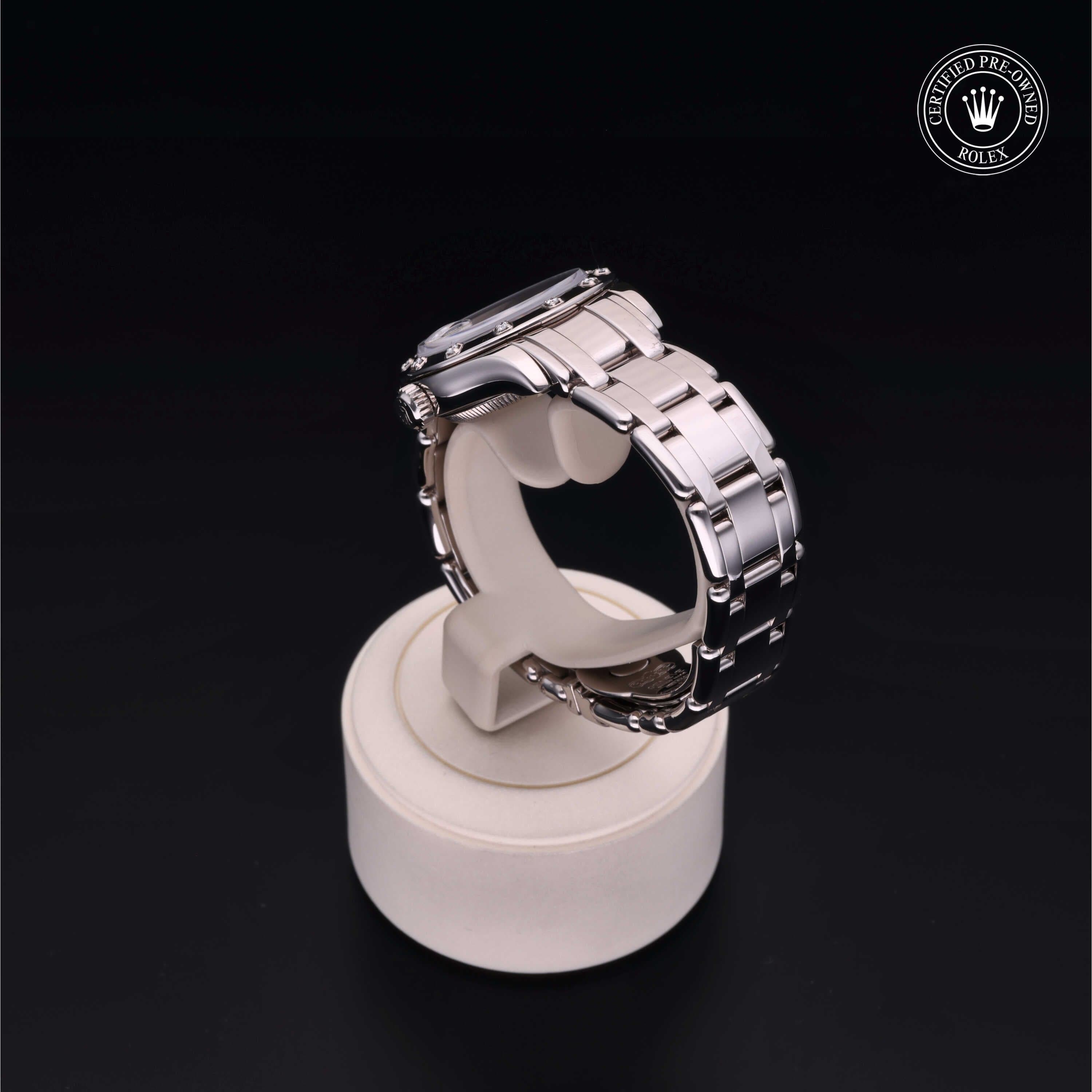Silver metallic wristwatch displayed on a round stand, set against a black background.