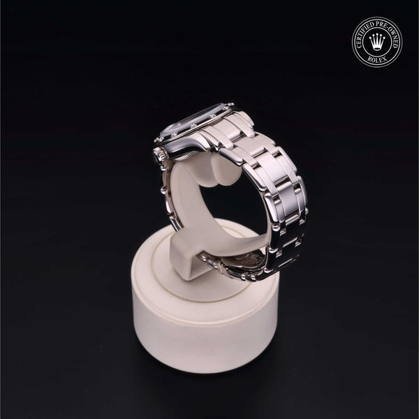 Silver metallic wristwatch displayed on a round stand, set against a black background.