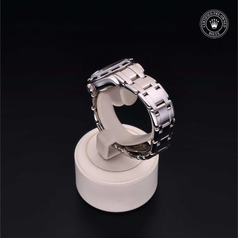 Silver metallic wristwatch displayed on a round stand, set against a black background.