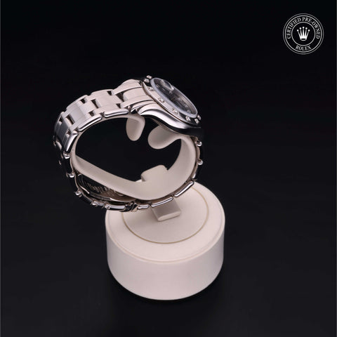 A silver Rolex watch on a stand, positioned sideways against a dark background.