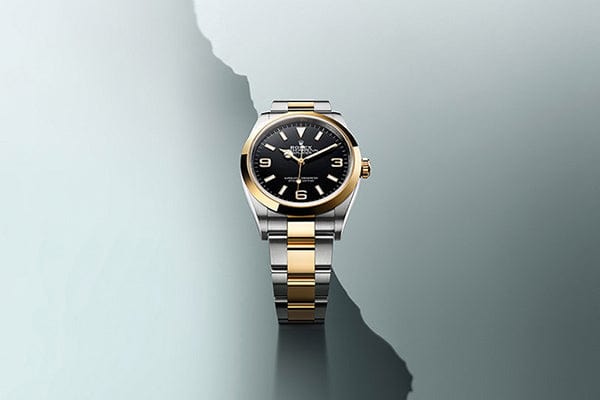 A sleek, elegant wristwatch with a gold and silver metal band is displayed against a minimalist, abstract background. The watch features a black dial with gold indices and numerals, and a gold bezel, exuding a classic and luxurious feel.