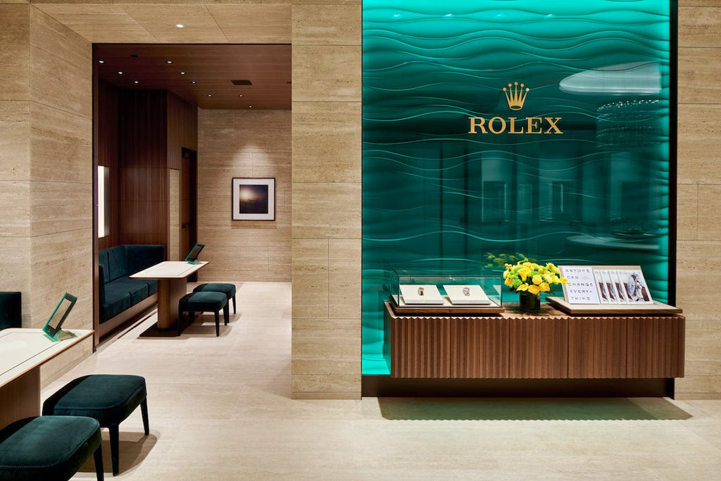 A modern Rolex store interior featuring a green illuminated wave-patterned wall with the Rolex logo, a wooden display counter with watches and yellow flowers, and elegant seating areas with green upholstered benches. Soft lighting enhances the luxurious ambiance.