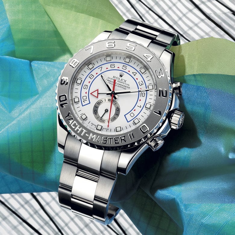 A silver wristwatch with a white dial and red, blue, and black details rests on a colorful fabric, placed on a wooden surface.
