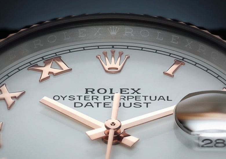 Close-up view of a Rolex Oyster Perpetual Datejust watch face. Roman numerals, the Rolex crown logo at the 12 o'clock position, and the brand name are visible. The date window shows the 28th, magnified by a cyclops lens.