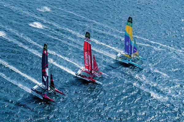 Three sailboats racing on a blue water surface with colorful sails.
