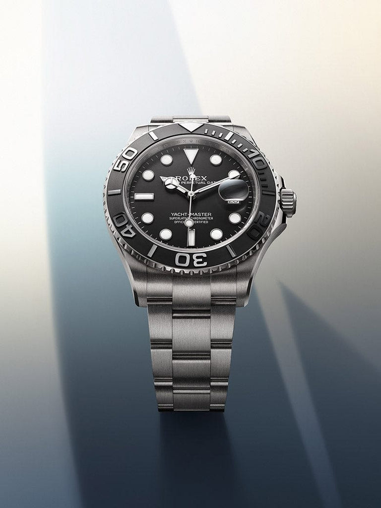A luxury wristwatch with a stainless steel band and a black dial is displayed prominently. The watch has a rotating bezel with white markings, luminous hour markers, and a date function. The background is gradient, transitioning from soft blues to pale yellows.