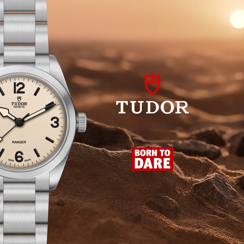 A Tudor Ranger watch with a silver metal bracelet and case, cream dial, and black numerals, shown against a desert landscape background with the Tudor logo and 'Born to Dare' text.